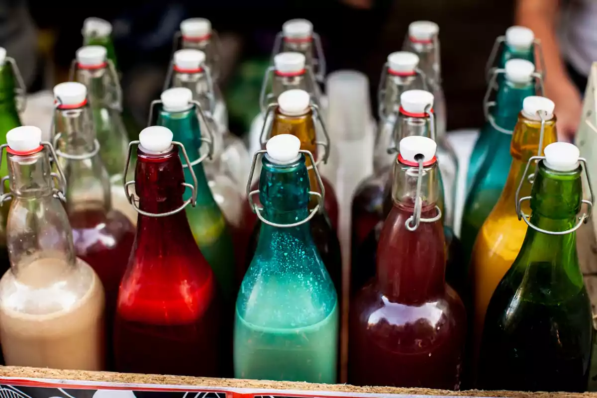 Botellas de vidrio con diferentes bebidas de colores vibrantes y tapas blancas alineadas en una mesa Botellas de vidrio con diferentes bebidas de colores vibrantes y tapas blancas alineadas en una mesa