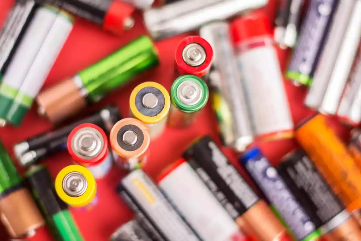 Varios tipos de pilas alcalinas y recargables de diferentes colores y tamaños sobre una superficie roja Varios tipos de pilas alcalinas y recargables de diferentes colores y tamaños sobre una superficie roja