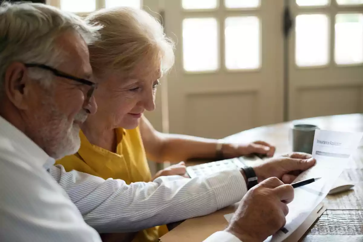 Pareja de personas mayores revisando documentos y usando una calculadora en una mesa