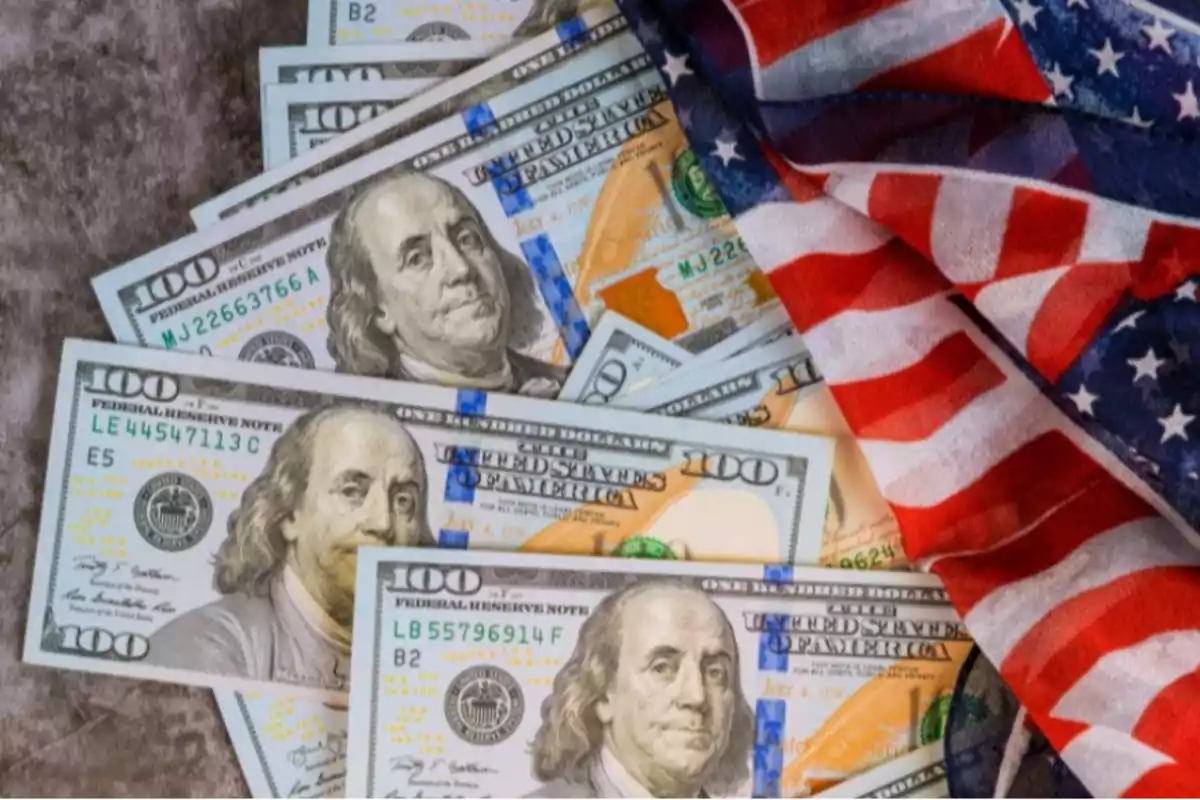 Billetes de cien dólares estadounidenses junto a una bandera de Estados Unidos Billetes de cien dólares estadounidenses junto a una bandera de Estados Unidos