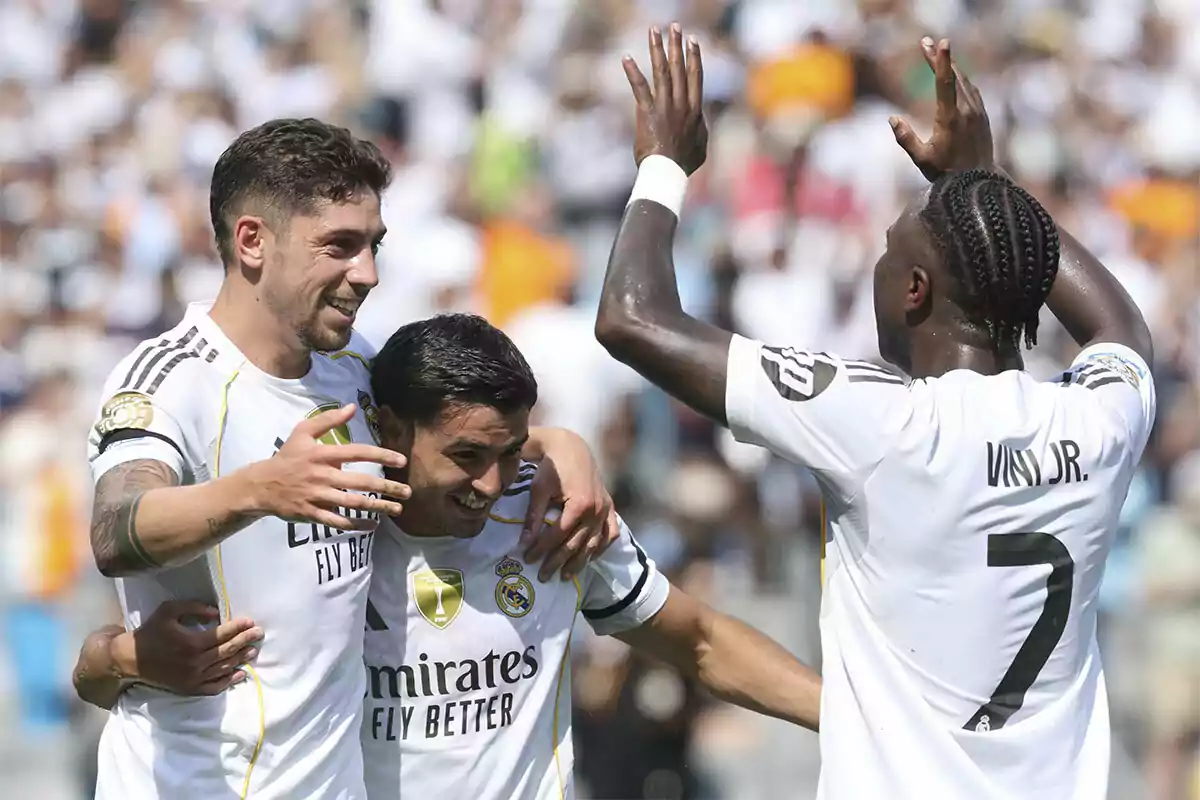 Tres jugadores del Real Madrid celebran un gol abrazándose y sonriendo en el campo de fútbol durante un partido Tres jugadores del Real Madrid celebran un gol abrazándose y sonriendo en el campo de fútbol durante un partido