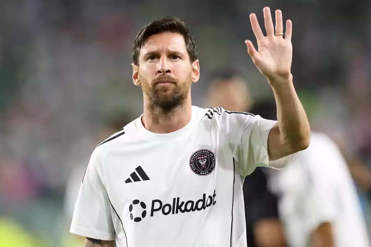 Soccer player wearing a white Inter Miami jersey raising his hand in greeting at a stadium Soccer player wearing a white Inter Miami jersey raising his hand in greeting at a stadium