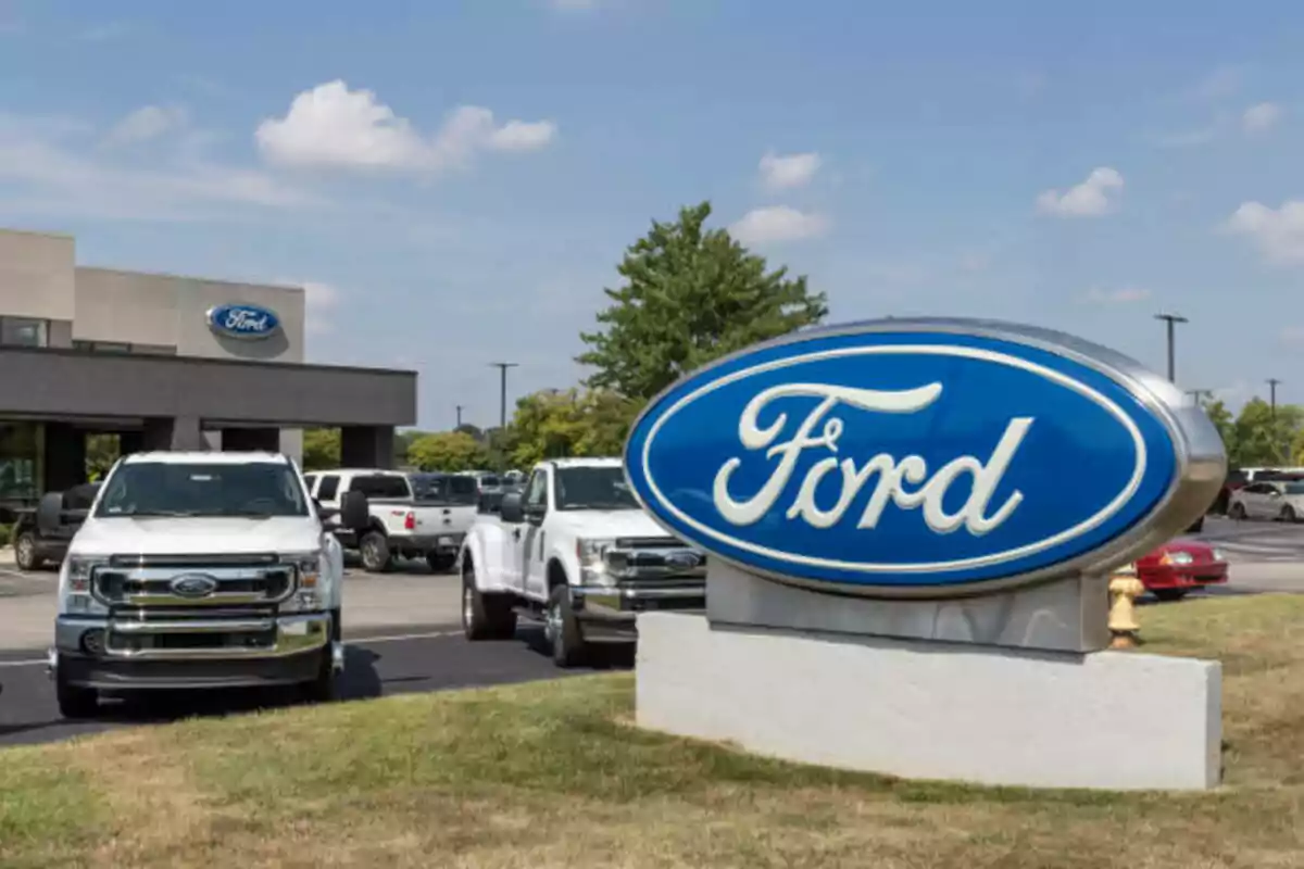 Concesionario de autos Ford con varias camionetas blancas estacionadas y un gran letrero azul de la marca en primer plano Concesionario de autos Ford con varias camionetas blancas estacionadas y un gran letrero azul de la marca en primer plano