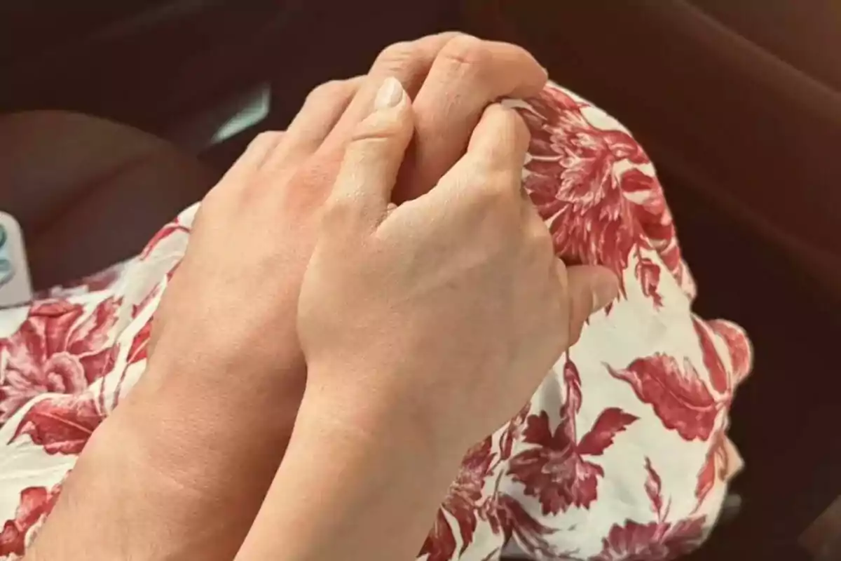 Manos entrelazadas sobre un vestido blanco con flores rojas Manos entrelazadas sobre un vestido blanco con flores rojas