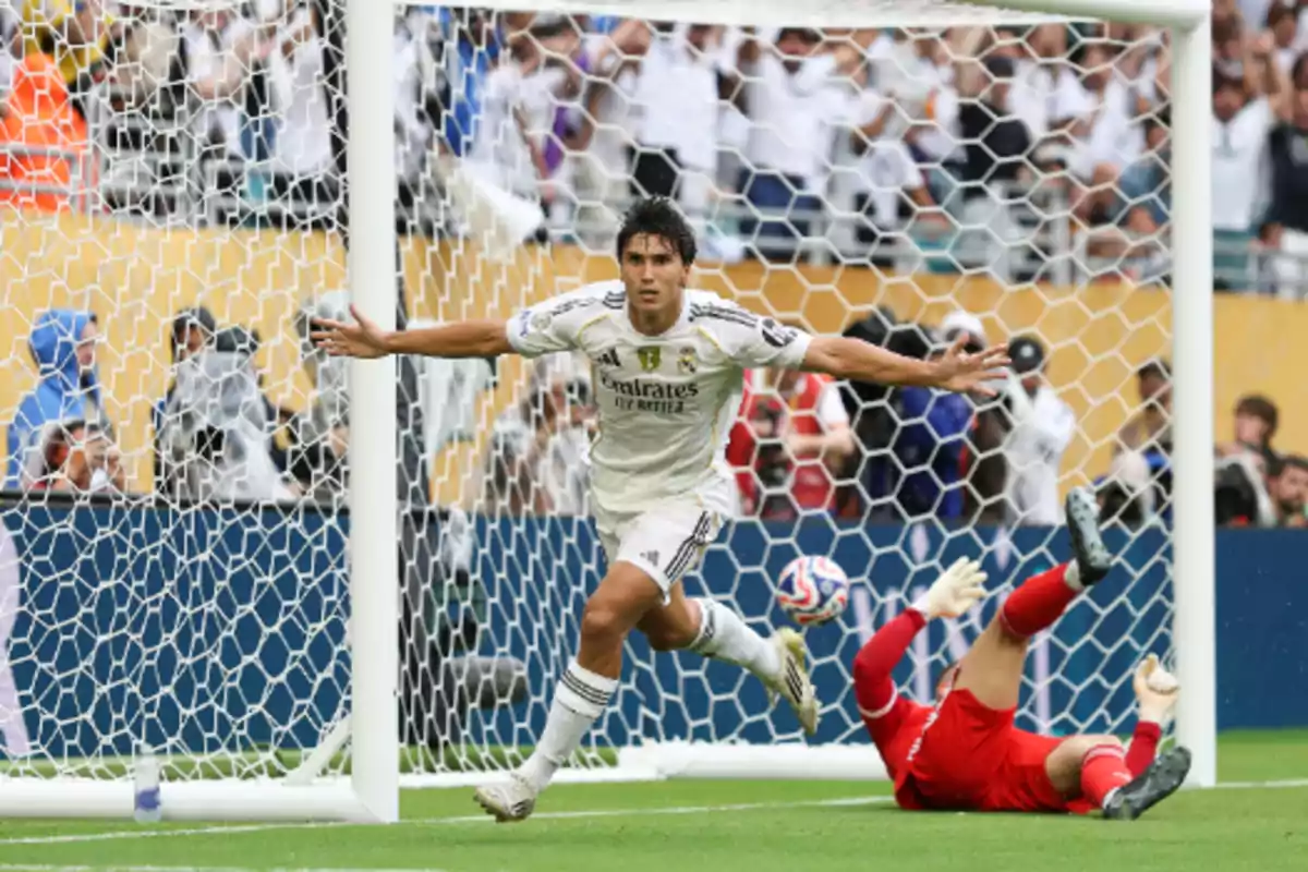 Real Madrid player celebrating a goal with arms outstretched while the opposing goalkeeper is on the ground inside the box