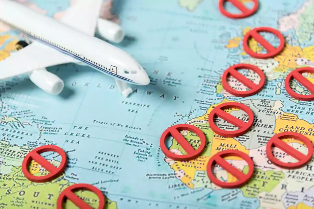 Avión de juguete sobre un mapa con varios símbolos de prohibido en diferentes países Avión de juguete sobre un mapa con varios símbolos de prohibido en diferentes países