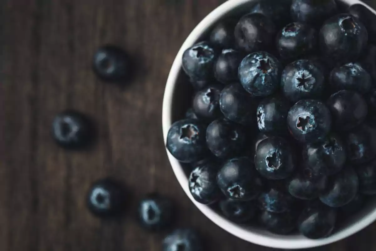White bowl filled with fresh blueberries on a dark wooden table White bowl filled with fresh blueberries on a dark wooden table