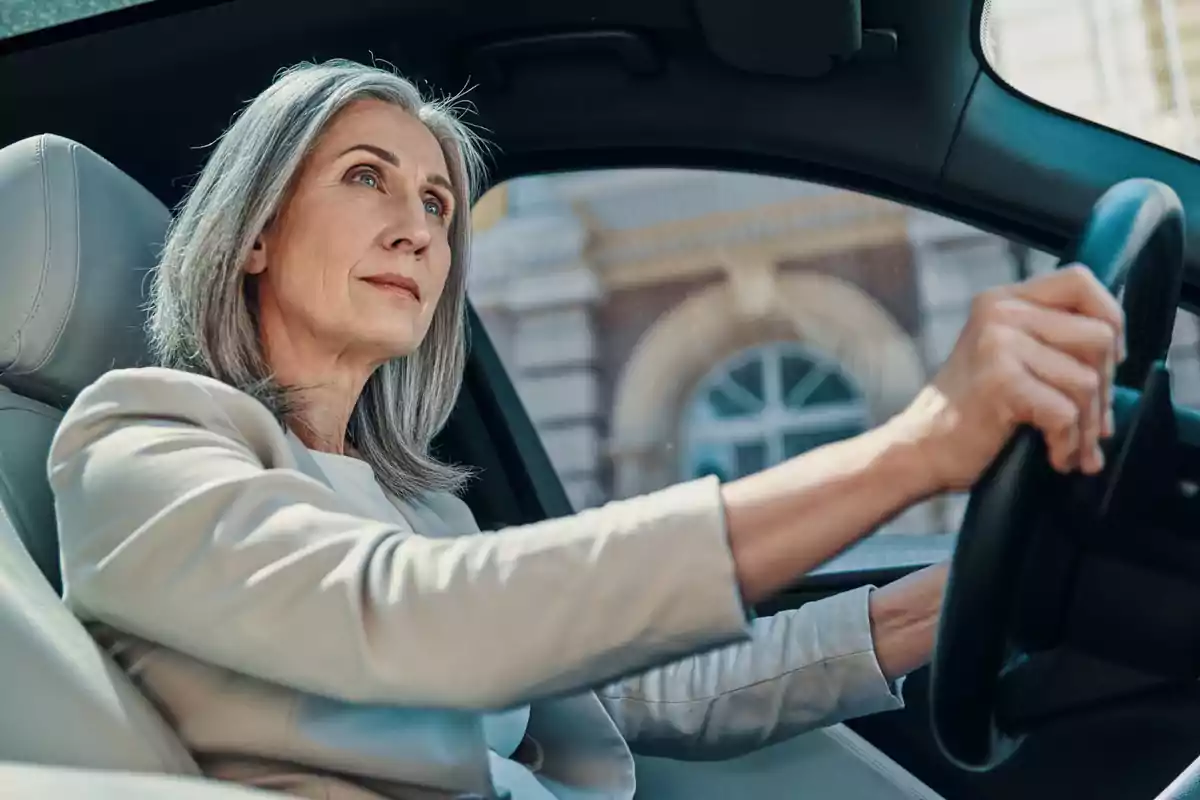 Mujer de cabello canoso conduciendo un automóvil y mirando hacia adelante con expresión seria