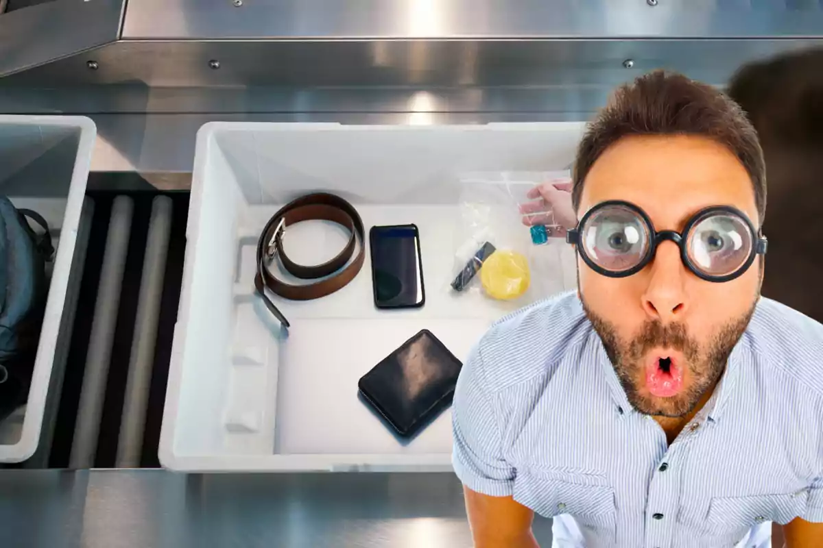 Hombre con gafas grandes y expresión de sorpresa junto a una bandeja de control de seguridad en el aeropuerto con objetos personales como cinturón, teléfono, cartera y líquidos.