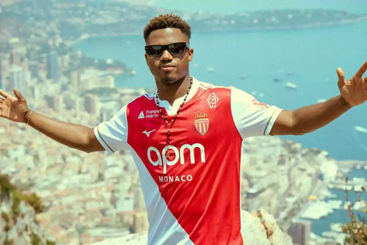 Hombre con gafas de sol y camiseta del AS Monaco posando con los brazos abiertos frente a una vista panorámica de una ciudad costera Hombre con gafas de sol y camiseta del AS Monaco posando con los brazos abiertos frente a una vista panorámica de una ciudad costera