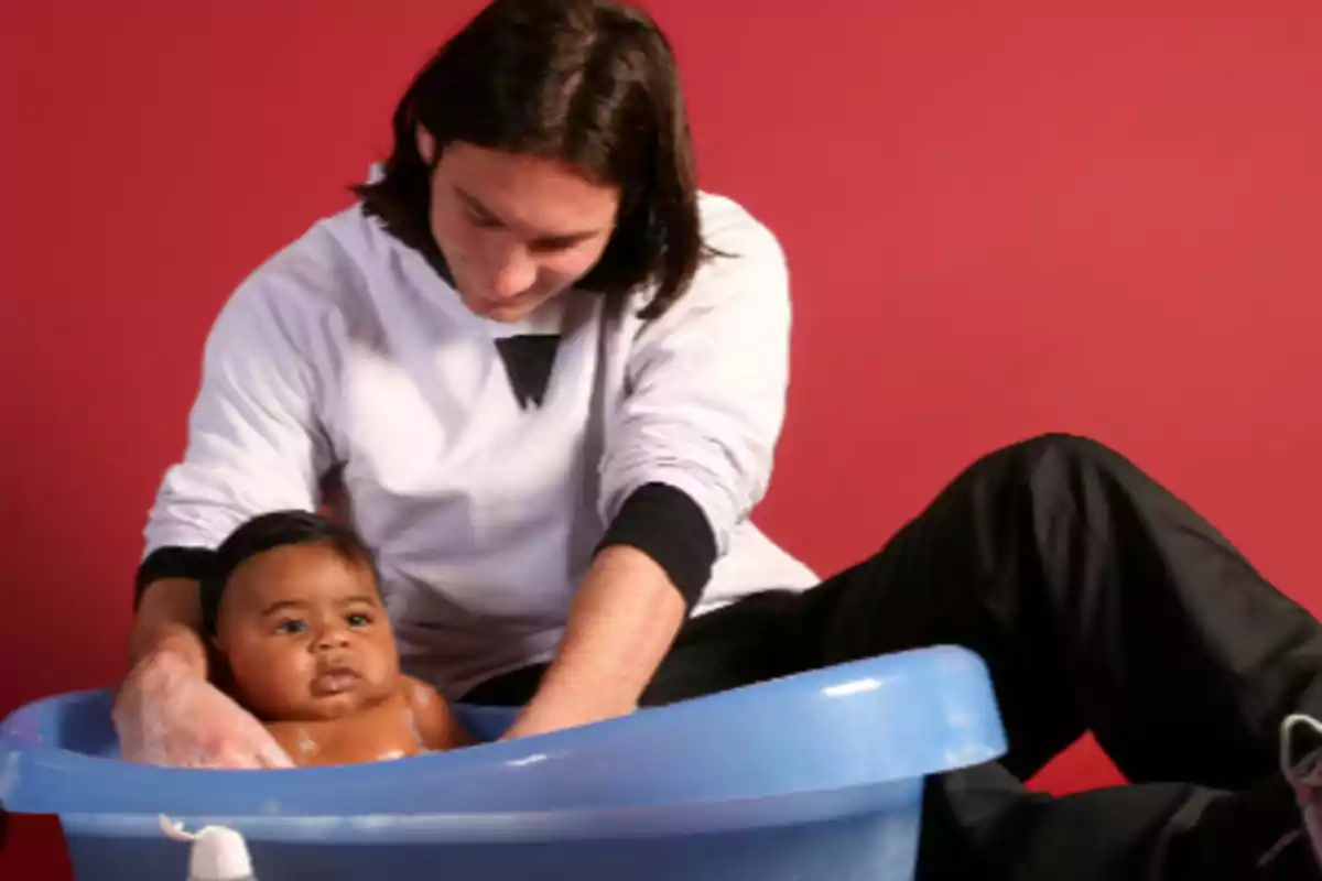 Person bathing a baby in a blue tub in front of a red wall Person bathing a baby in a blue tub in front of a red wall