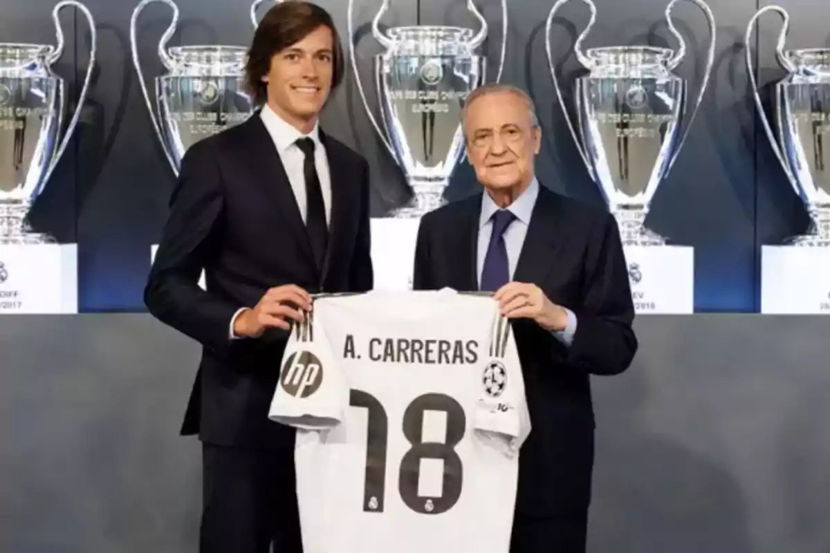 Two men in suits hold a soccer jersey with the name A. Carreras and the number 18 in front of several large trophies in the background. Two men in suits hold a soccer jersey with the name A. Carreras and the number 18 in front of several large trophies in the background.