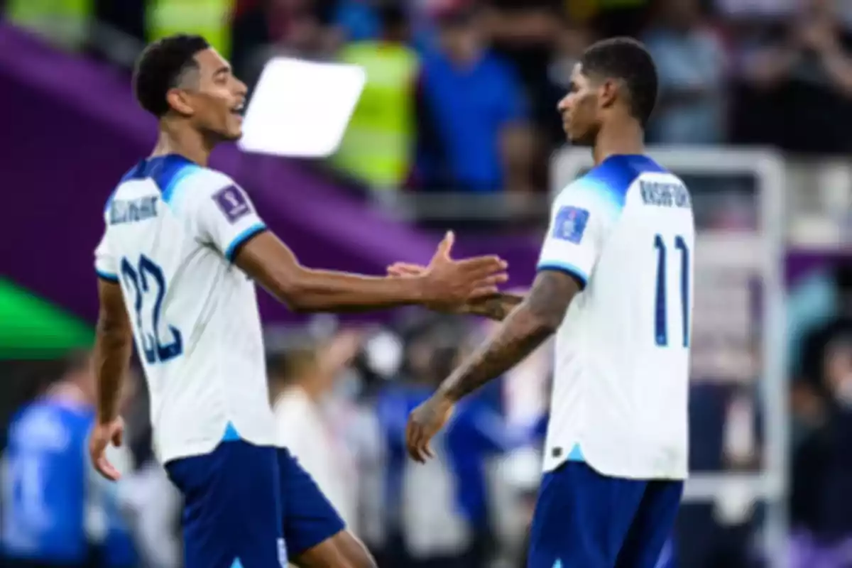 Two players in white and blue uniforms celebrate on the field during a match. Two players in white and blue uniforms celebrate on the field during a match.