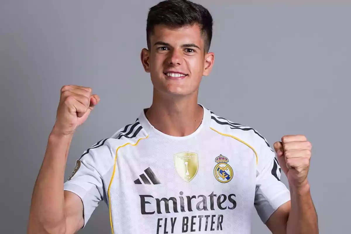 Joven con camiseta del Real Madrid celebrando con los puños en alto y sonriendo frente a un fondo gris Joven con camiseta del Real Madrid celebrando con los puños en alto y sonriendo frente a un fondo gris