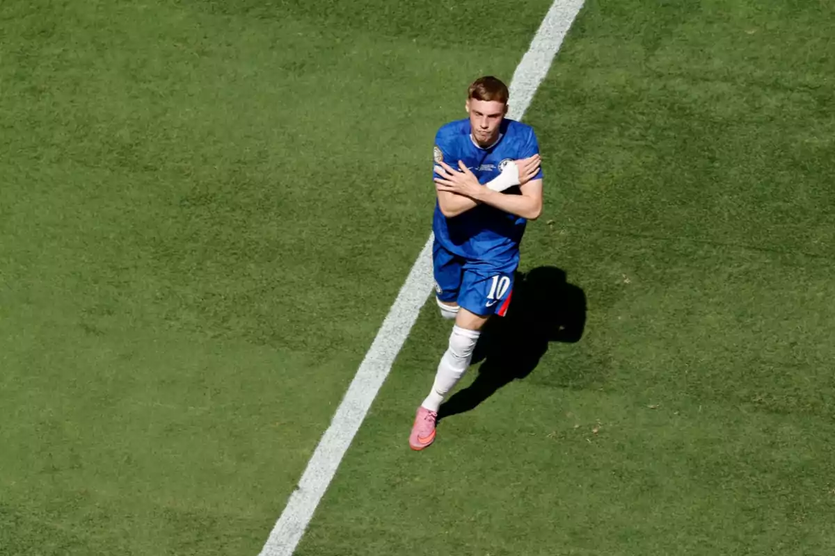 Futbolista con uniforme azul celebrando un gol con los brazos cruzados sobre el pecho en una cancha de pasto Futbolista con uniforme azul celebrando un gol con los brazos cruzados sobre el pecho en una cancha de pasto