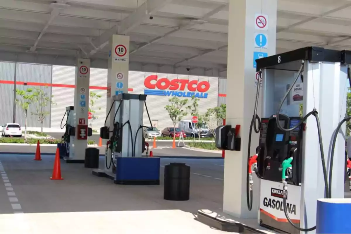 Estación de gasolina de Costco con varias bombas de combustible y conos naranjas bajo un techo, con el edificio de Costco al fondo Estación de gasolina de Costco con varias bombas de combustible y conos naranjas bajo un techo, con el edificio de Costco al fondo