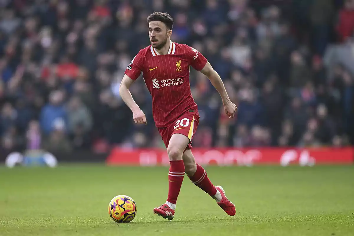 Futbolista del Liverpool con uniforme rojo controla el balón durante un partido en un estadio lleno de espectadores Futbolista del Liverpool con uniforme rojo controla el balón durante un partido en un estadio lleno de espectadores