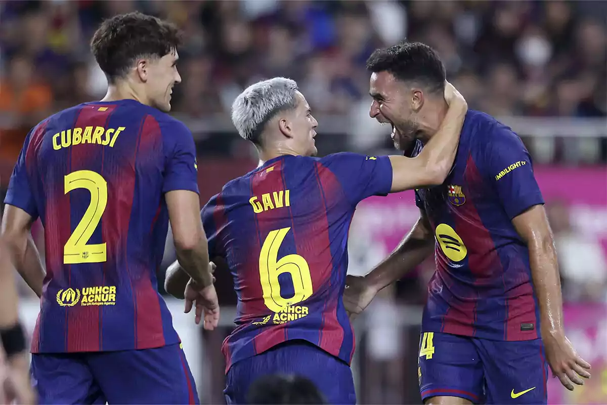 Tres jugadores del FC Barcelona celebran un gol en el campo, luciendo el uniforme azulgrana y mostrando alegría y compañerismo. Tres jugadores del FC Barcelona celebran un gol en el campo, luciendo el uniforme azulgrana y mostrando alegría y compañerismo.
