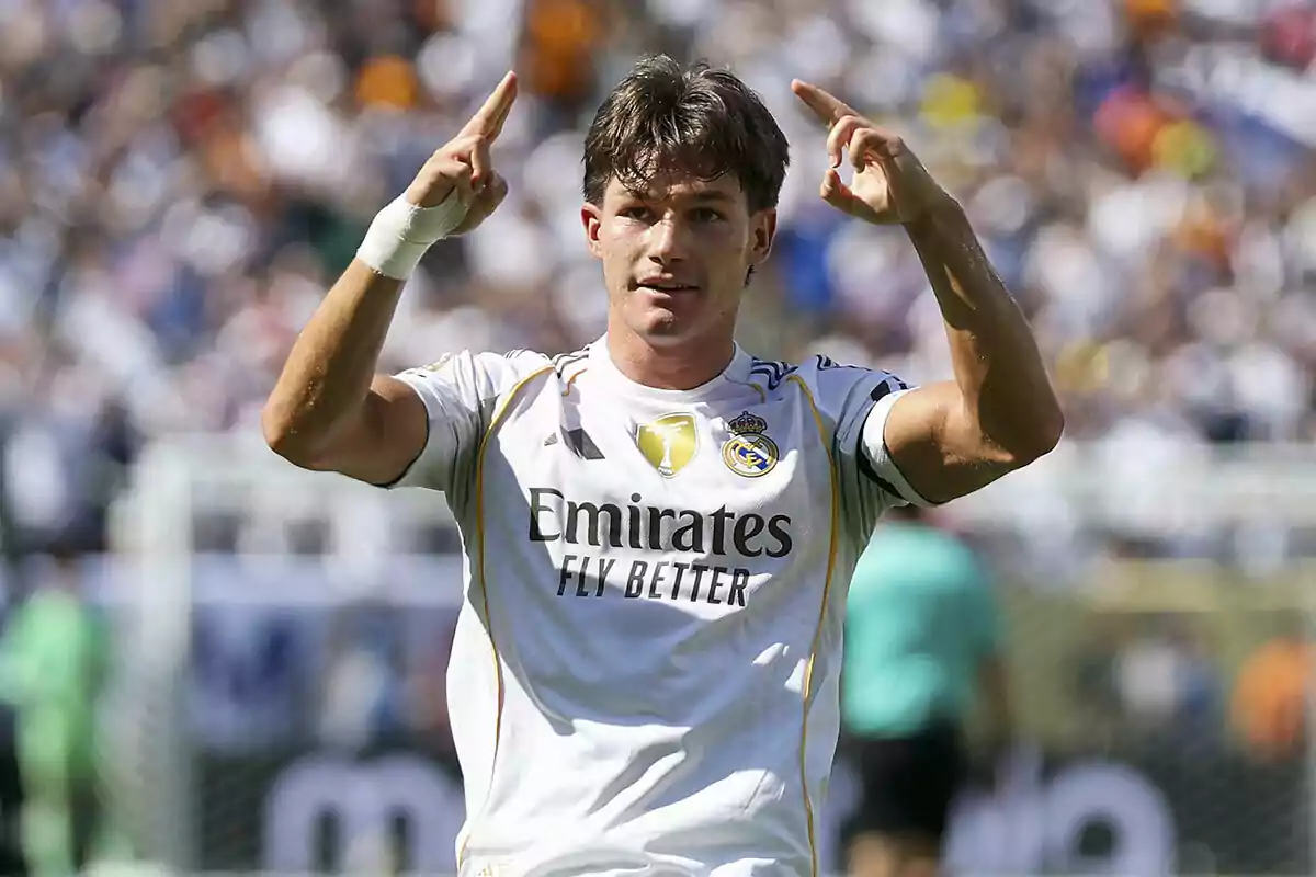 Futbolista del Real Madrid celebrando un gol con ambas manos señalando hacia arriba en un estadio lleno de aficionados Futbolista del Real Madrid celebrando un gol con ambas manos señalando hacia arriba en un estadio lleno de aficionados