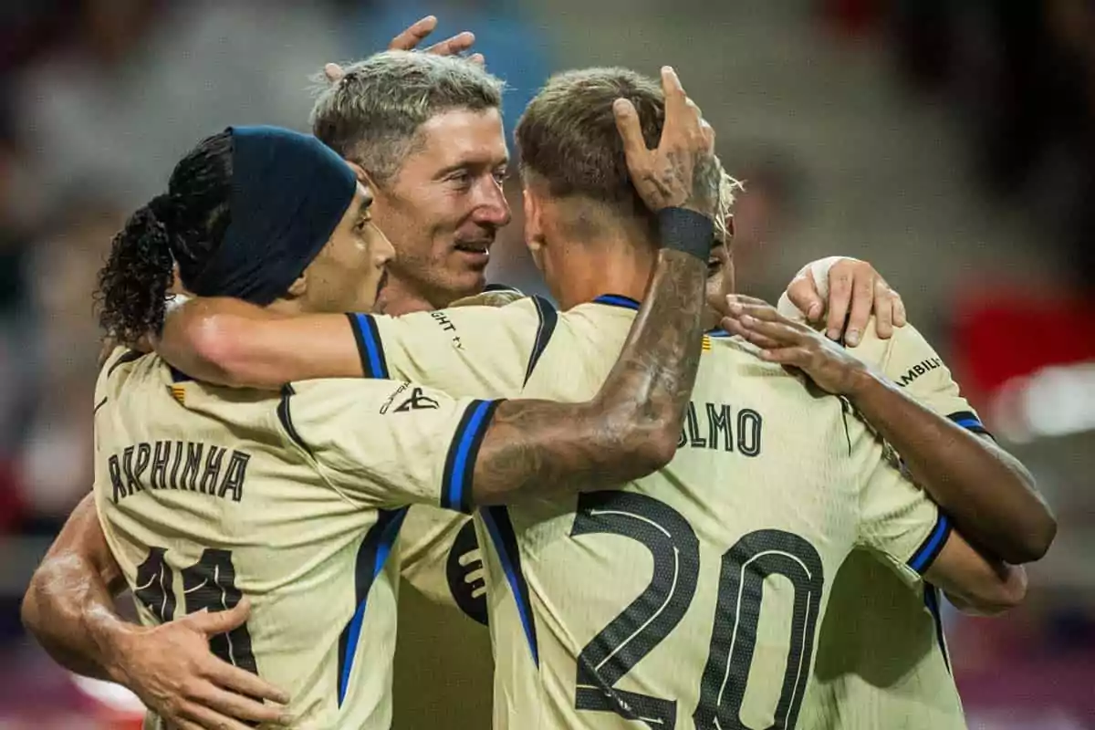 Tres futbolistas con uniforme beige se abrazan celebrando un gol en un estadio Tres futbolistas con uniforme beige se abrazan celebrando un gol en un estadio