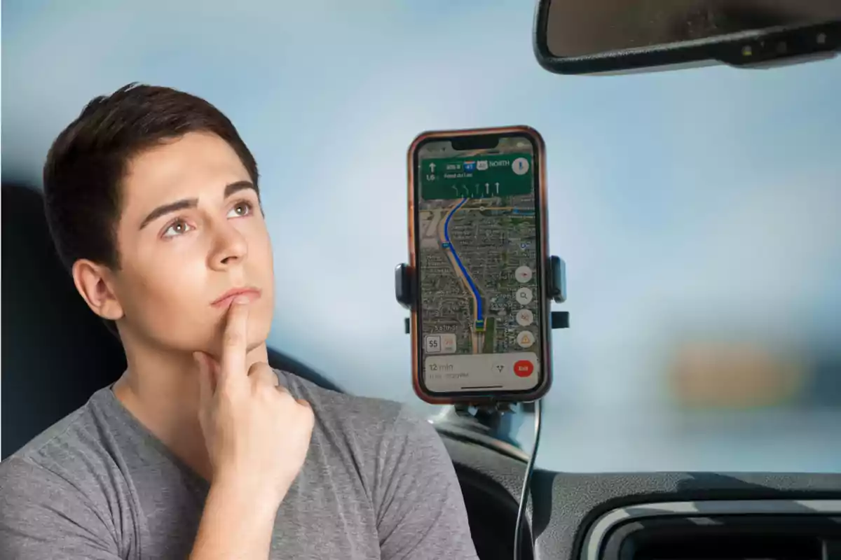 Thoughtful young man inside a car looking at a phone with a maps app open on the windshield mount Thoughtful young man inside a car looking at a phone with a maps app open on the windshield mount