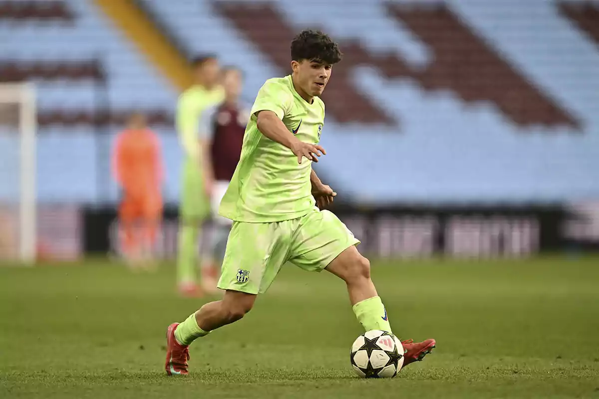 Joven futbolista con uniforme verde fosforescente controla el balón durante un partido en un estadio de fútbol. Joven futbolista con uniforme verde fosforescente controla el balón durante un partido en un estadio de fútbol.