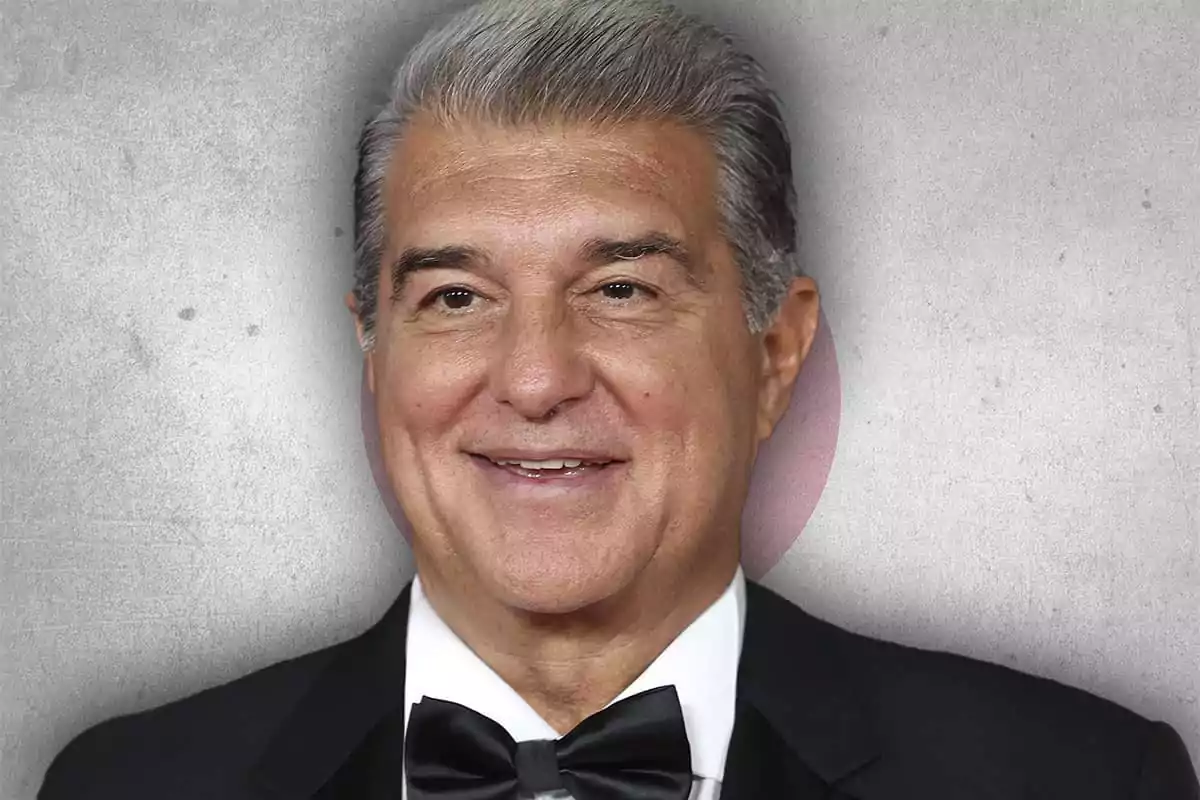 Hombre de cabello canoso con esmoquin y pajarita negra sonriendo frente a un fondo gris