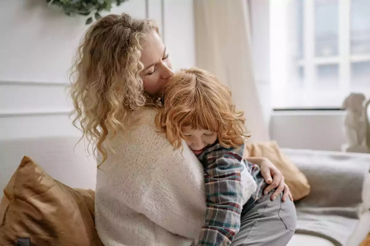 Woman hugging and kissing a small child on a sofa in a brightly lit living room Woman hugging and kissing a small child on a sofa in a brightly lit living room