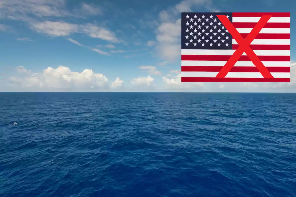 Vista del océano bajo un cielo parcialmente nublado con una bandera de Estados Unidos en la esquina superior derecha tachada con una X roja