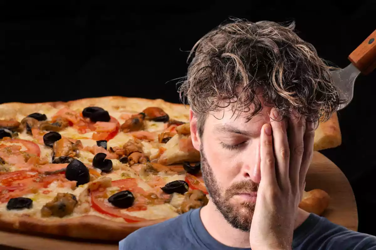 Hombre con expresión de malestar cubriéndose el rostro con la mano frente a una pizza sobre una pala