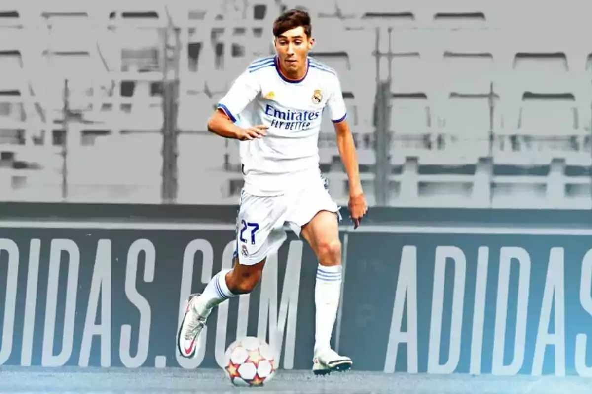 Jugador de fútbol con uniforme blanco del Real Madrid controlando el balón en un estadio con publicidad de Adidas al fondo Jugador de fútbol con uniforme blanco del Real Madrid controlando el balón en un estadio con publicidad de Adidas al fondo