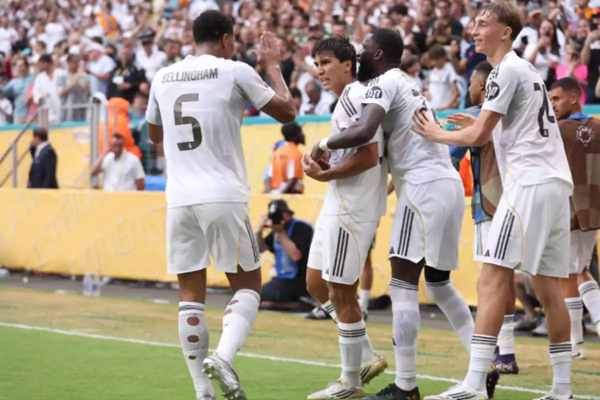Soccer players in white uniforms celebrate a goal on the field in front of a crowd of fans in the stands.
