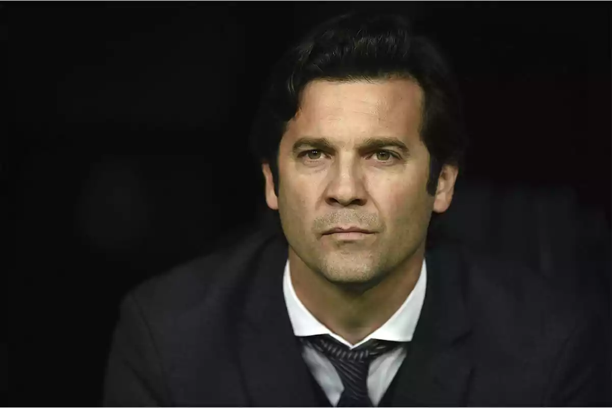 Hombre de cabello oscuro con expresión seria vistiendo traje y corbata frente a un fondo oscuro Hombre de cabello oscuro con expresión seria vistiendo traje y corbata frente a un fondo oscuro
