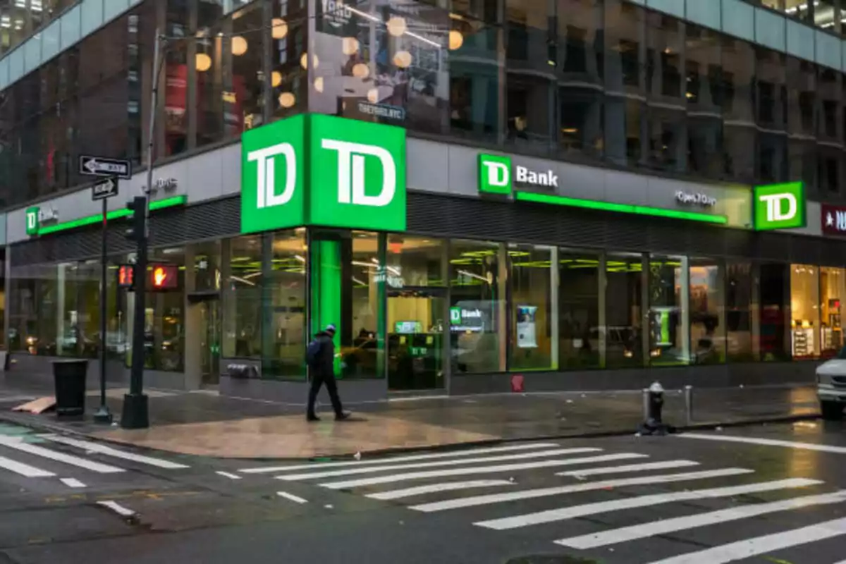 Sucursal de TD Bank en una esquina de ciudad con una persona cruzando la calle en un día nublado Sucursal de TD Bank en una esquina de ciudad con una persona cruzando la calle en un día nublado