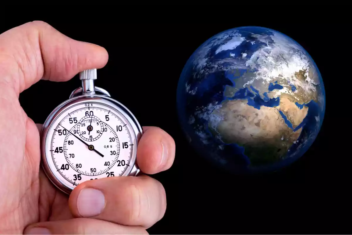 Mano sosteniendo un cronómetro plateado frente a una imagen del planeta Tierra sobre fondo negro