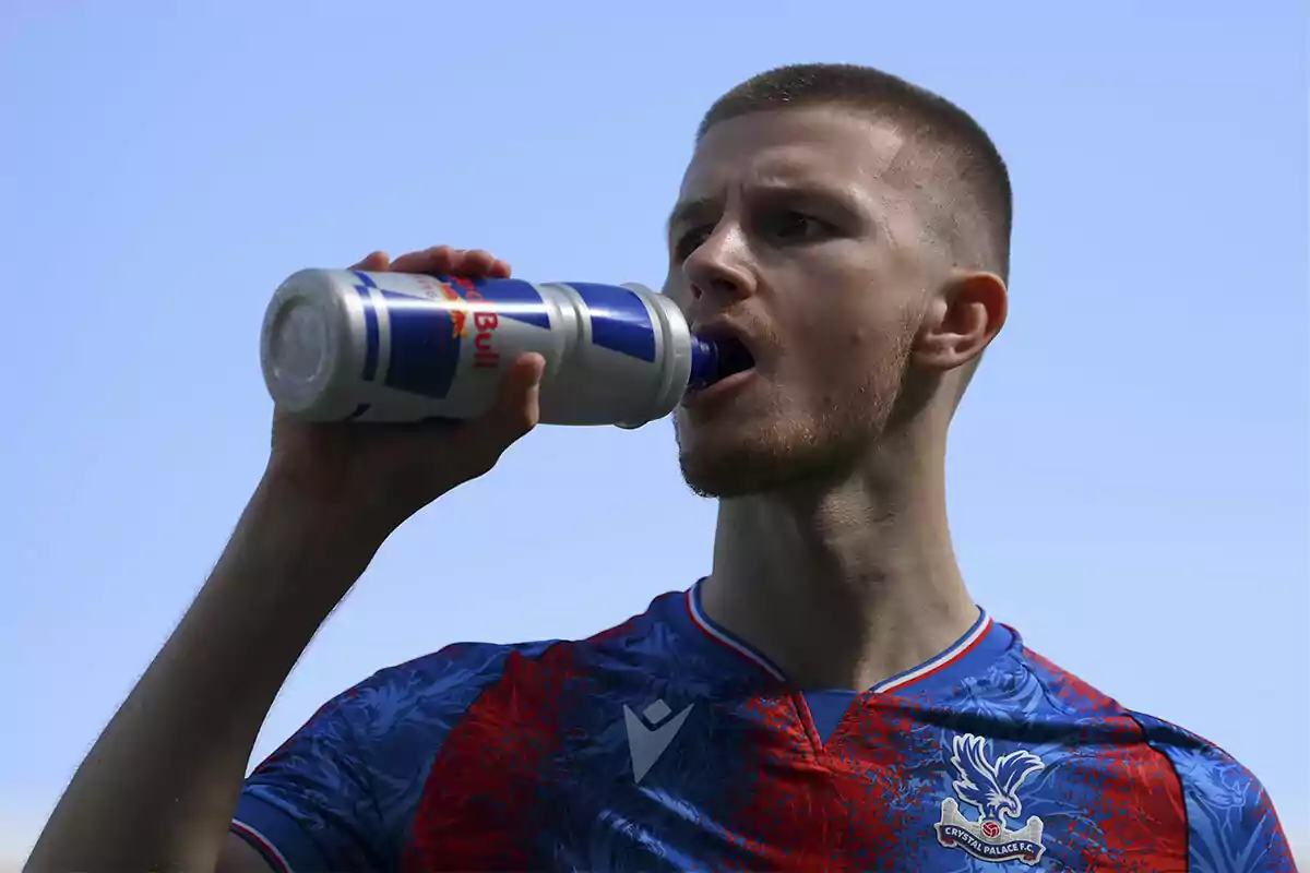 Soccer player wearing a Crystal Palace jersey drinking from a Red Bull bottle under the clear sky Soccer player wearing a Crystal Palace jersey drinking from a Red Bull bottle under the clear sky