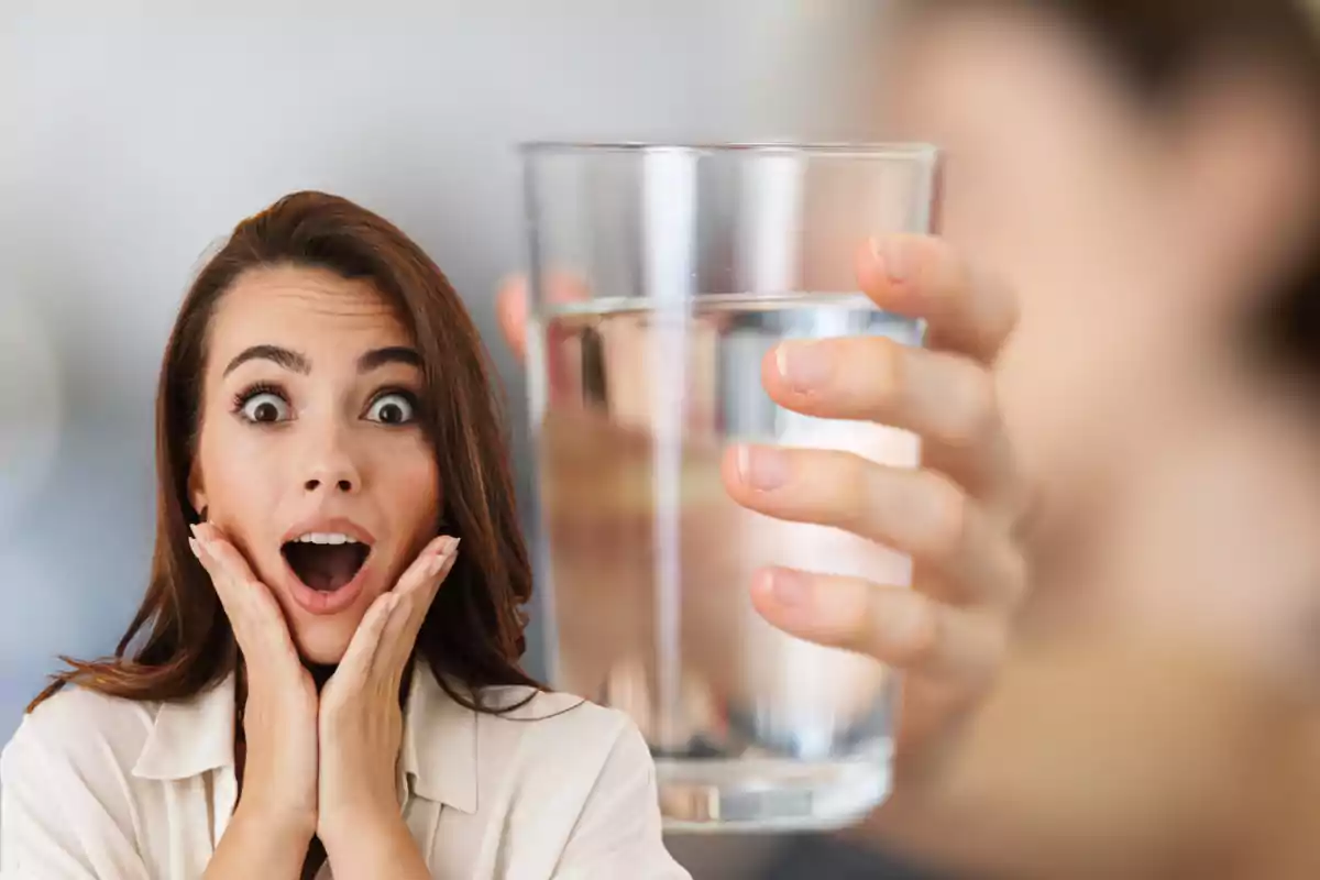 Mujer con expresión de sorpresa junto a un vaso de agua sostenido por una mano