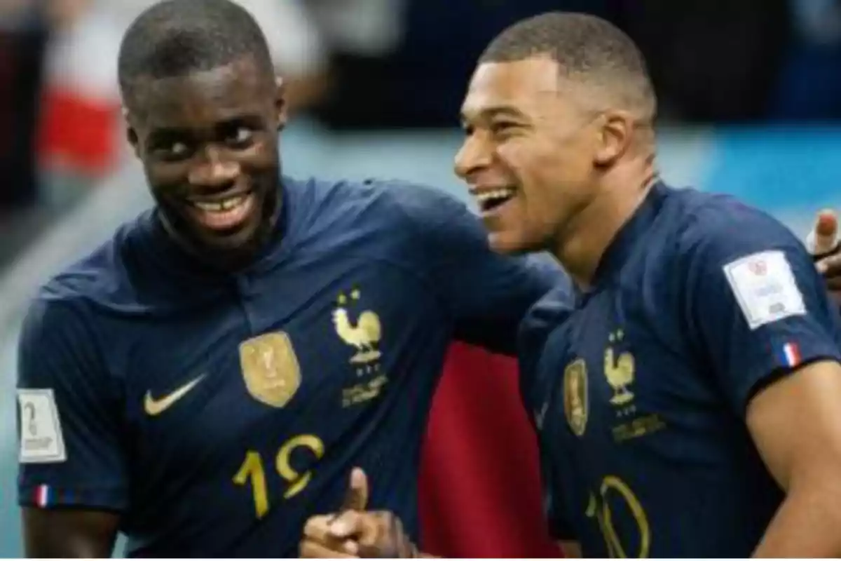 Two players from the French national team smile and celebrate together on the field during a match. Two players from the French national team smile and celebrate together on the field during a match.