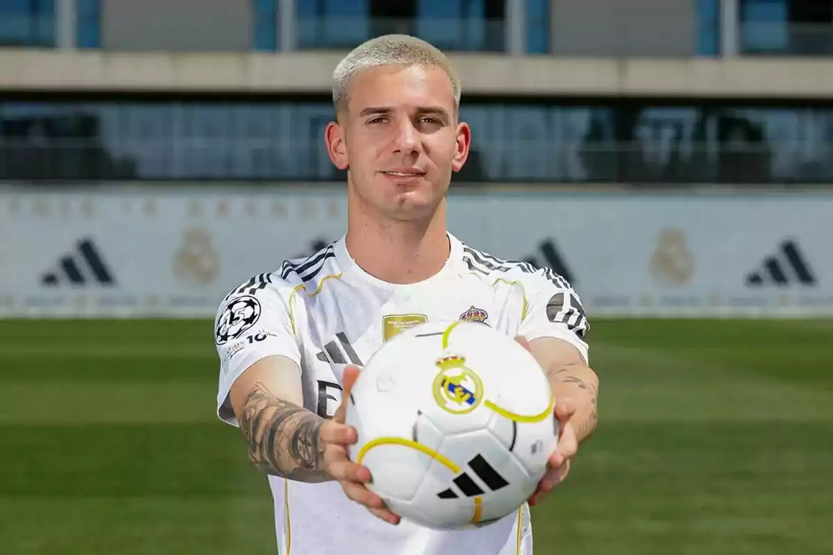 Futbolista con camiseta blanca del Real Madrid sosteniendo un balón en primer plano en un campo de entrenamiento Futbolista con camiseta blanca del Real Madrid sosteniendo un balón en primer plano en un campo de entrenamiento