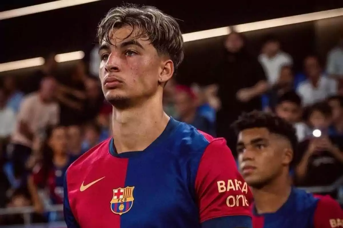 Young player in FC Barcelona uniform at a stadium, with a serious expression and blurred crowd in the background Young player in FC Barcelona uniform at a stadium, with a serious expression and blurred crowd in the background