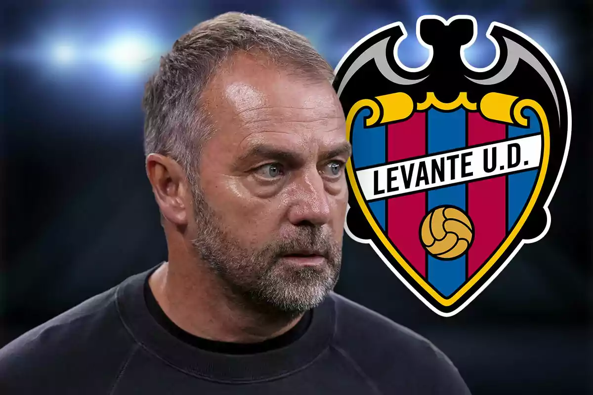 Short-haired, bearded man with a serious expression in front of the Levante UD crest