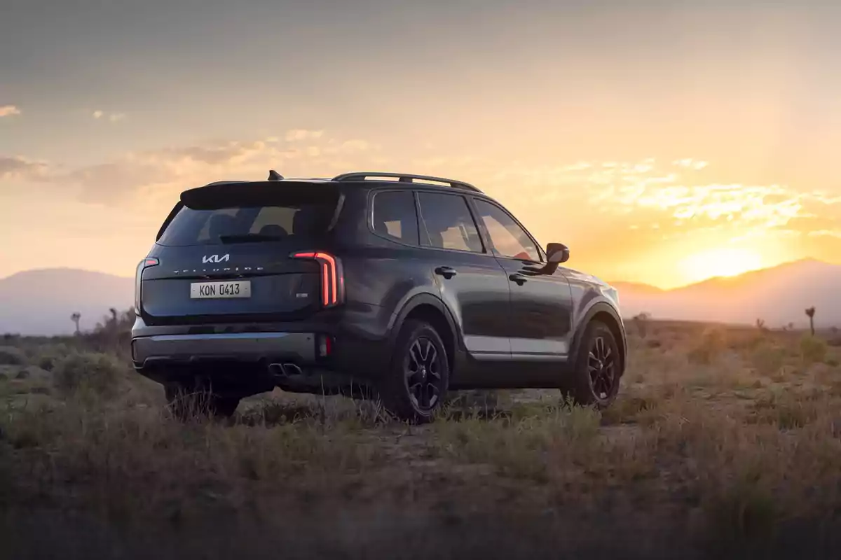 SUV negro estacionado en un paisaje desértico al atardecer con montañas al fondo y cielo anaranjado
