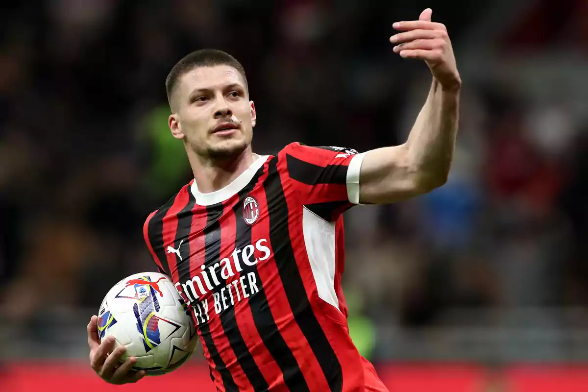 AC Milan player in a red and black uniform holding a ball during a match