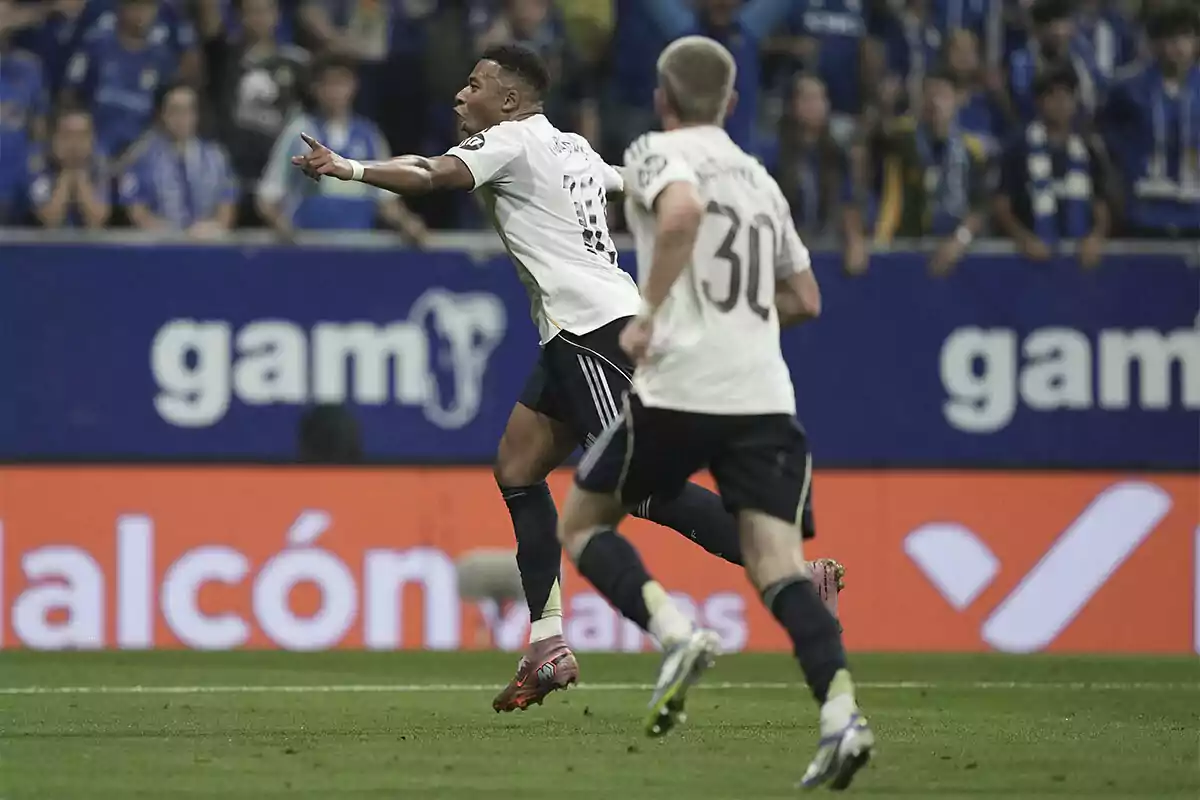 Dos futbolistas celebran un gol en un estadio lleno de aficionados mientras corren sobre el césped Dos futbolistas celebran un gol en un estadio lleno de aficionados mientras corren sobre el césped