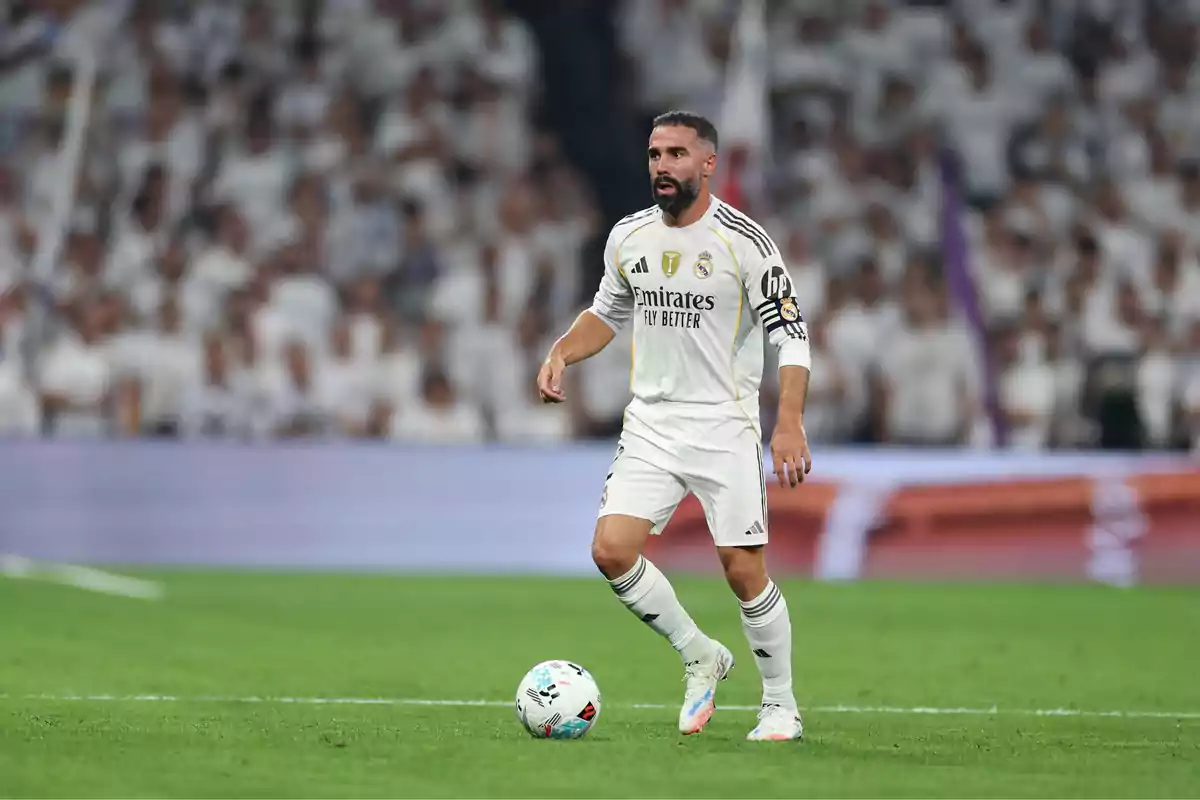 Futbolista del Real Madrid con uniforme blanco controlando el balón en el campo durante un partido con el público de fondo Futbolista del Real Madrid con uniforme blanco controlando el balón en el campo durante un partido con el público de fondo