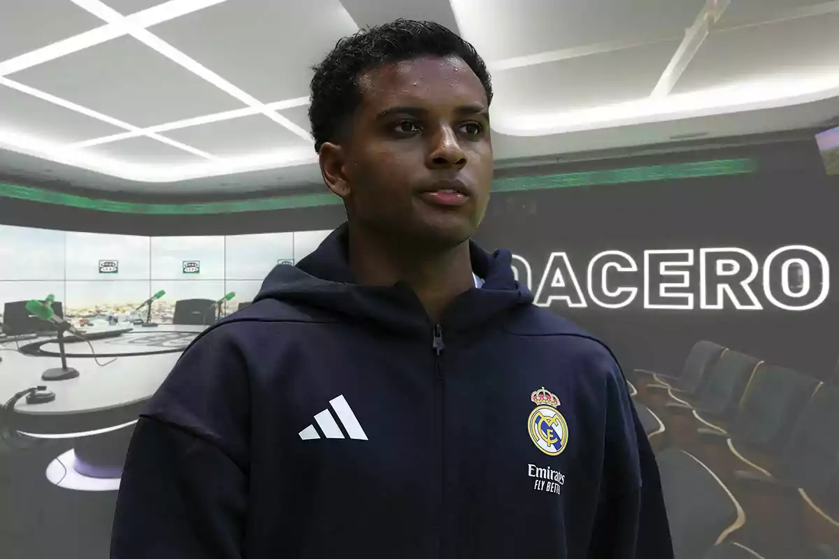 Un futbolista con sudadera del Real Madrid posando frente a un estudio de radio moderno con micrófonos verdes y la palabra Onda Cero iluminada en el fondo