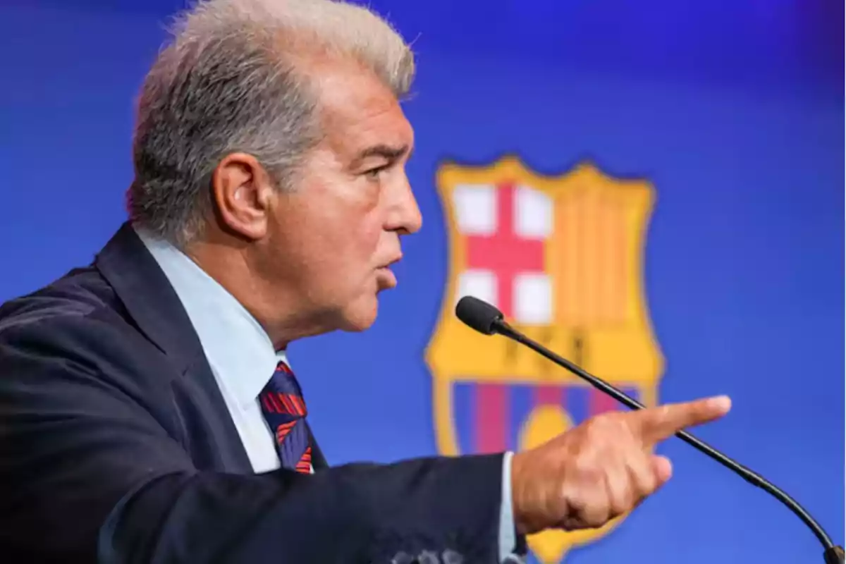 Gray-haired man speaking into a microphone and pointing with his finger in front of a background with the FC Barcelona crest. Gray-haired man speaking into a microphone and pointing with his finger in front of a background with the FC Barcelona crest.