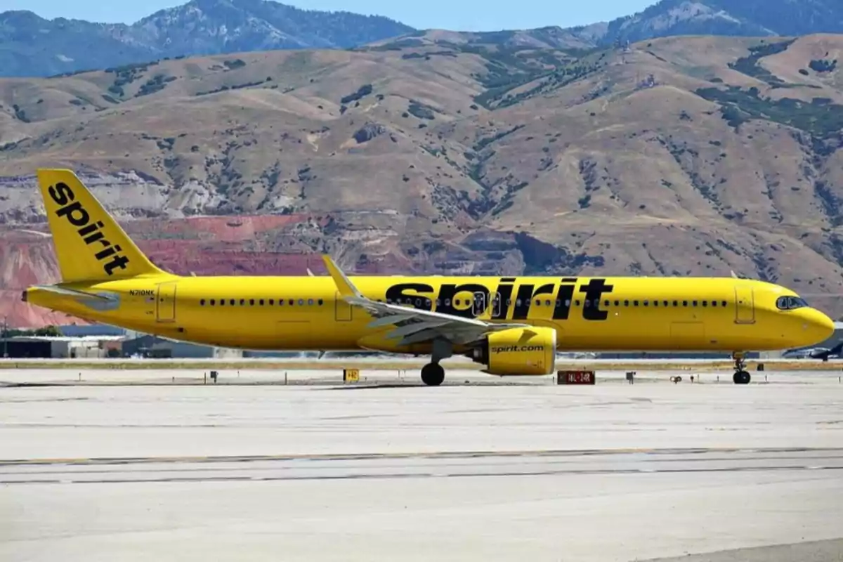 Avión amarillo de la aerolínea Spirit estacionado en una pista con montañas al fondo Avión amarillo de la aerolínea Spirit estacionado en una pista con montañas al fondo