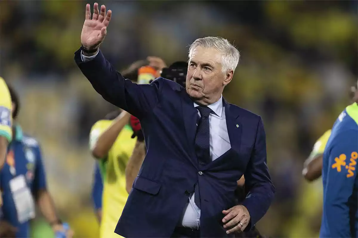 Gray-haired man in a blue suit waving his hand in a soccer stadium surrounded by people in sports uniforms Gray-haired man in a blue suit waving his hand in a soccer stadium surrounded by people in sports uniforms