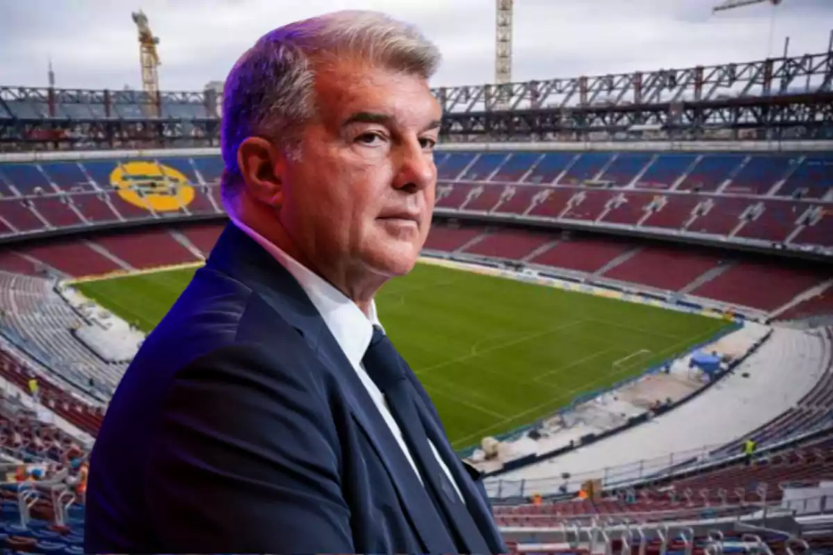 Gray-haired man in a dark suit in the foreground inside a soccer stadium under renovation